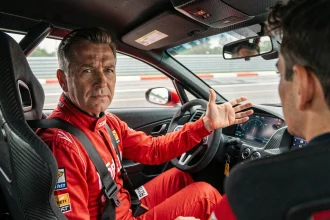 Instructeur de stage de pilotage en combinaison rouge expliquant une trajectoire à un élève dans un habitacle de voiture de circuit